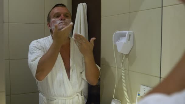 The man in front of a mirror causes shaving foam and shaves machine - Footage, Video
