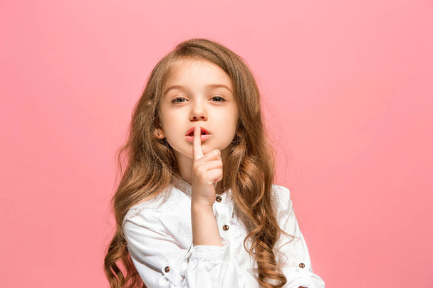 The young teen girl whispering a secret behind her hand over pink background - Photo, Image