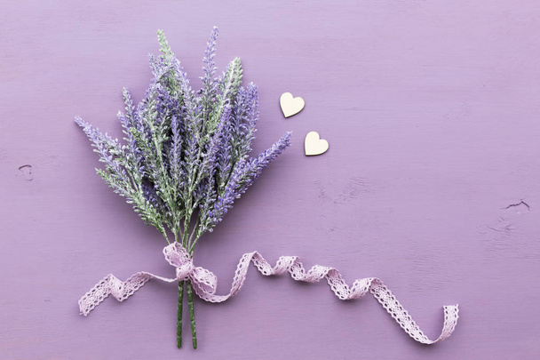 Lavender flower banded ribbon with bow on purple wooden background. Near two wooden hearts. - Fotografie, Obrázek