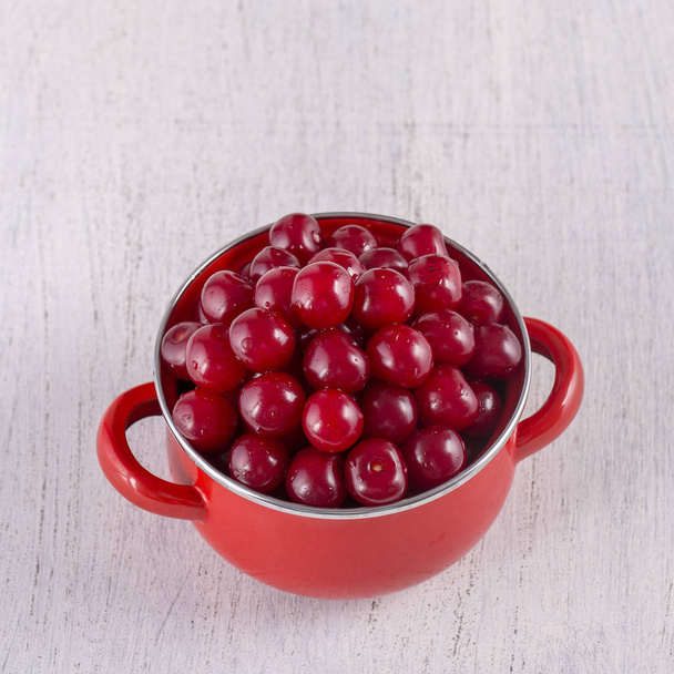 Red cherries in red enamel saucepan on white background, close up - Foto, imagen