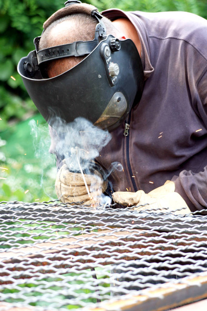 Welder welding  a metal part wearing standard protection equipment - 写真・画像