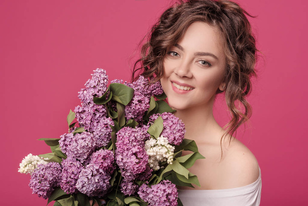 A young slender girl in stylish clothes is holding a bouquet of purple flowers. She is surprised at the gift she was given on a date. On a pink background with space for text - Zdjęcie, obraz