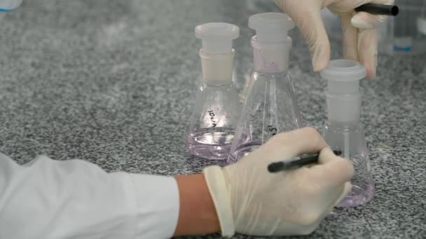 Scientist mark flasks with liquids in laboratory. Close-up. - Πλάνα, βίντεο
