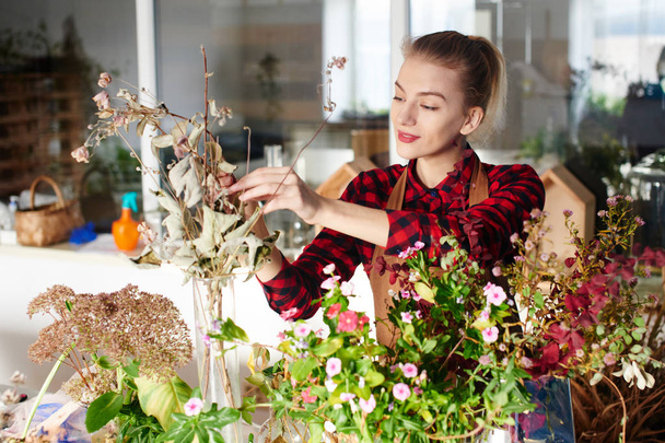 female redheaded florist taking care of plants in flower shop  - Foto, Bild