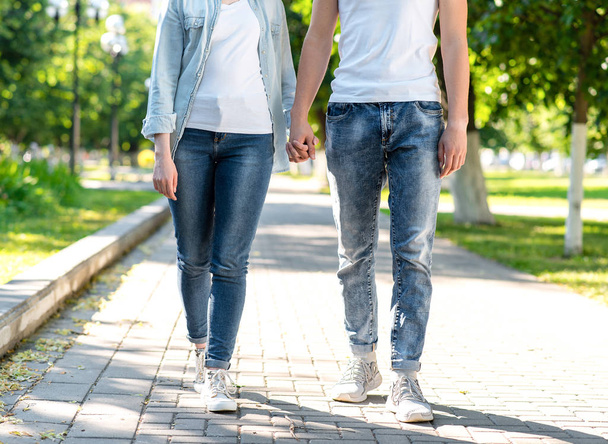 The guy with the girl. In summer in the park in nature. They walk along the sidewalk holding each others hands. Close-up on vacation. go ahead. Front view. - Foto, imagen