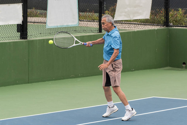 熟練高齢者中国テニス プレーヤーの試合でフォアハンド グランド ストロークに接続. - 写真・画像