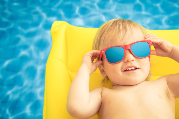 Funny baby boy on summer vacation. Child having fun in swimming pool - Foto, afbeelding
