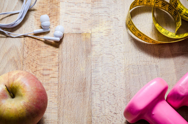 still life with pink weights and  yellow tape measure and an apple from above point of view. fitness. sport. concept. copy space centered - Photo, Image
