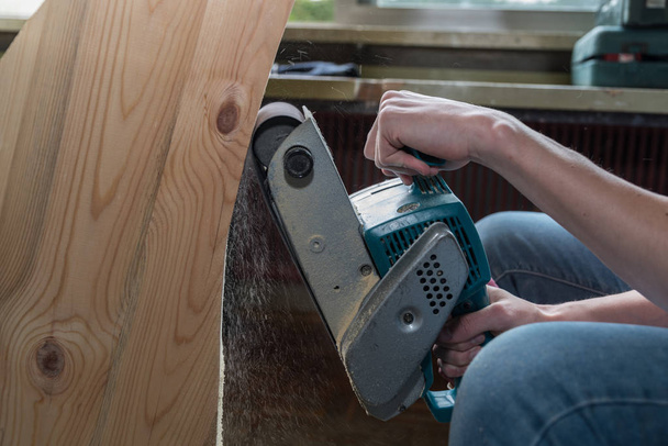 Carpinteiro está arrastando madeira com uma lixadeira na oficina - close-up
 - Foto, Imagem