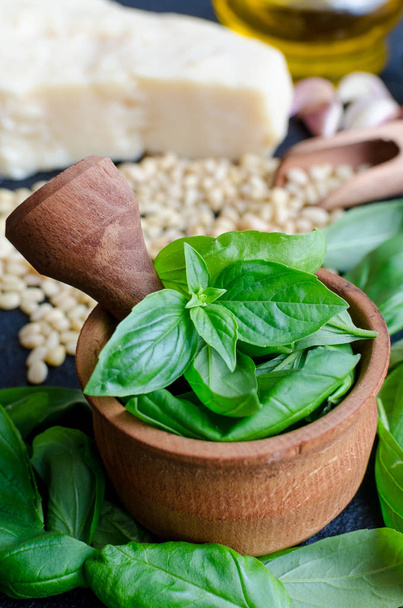 Fresh ingredients for pesto genovese sauce on black stone background. Basil leaves in mortar, Parmesan cheese, pine nuts, olive oil, garlic and salt. Traditional Italian cuisine. - Фото, зображення