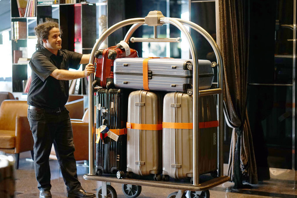 Chiudere molte valigie sul carrello bagagli dell'hotel in movimento dal ragazzo campana. Portabagagli o fattorino che portano la valigia degli ospiti con un furgoncino in camera d'albergo. Carrello Bagagli in hotel
. - Foto, immagini