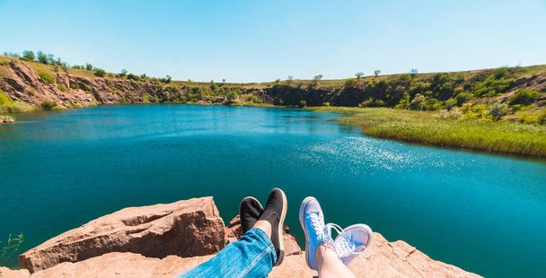 Travelers couple in sports shoes on a mountain near a river in the background of nature. Man and woman. A couple sits and makes their feet on a beautiful landscape with a river bank - Foto, imagen