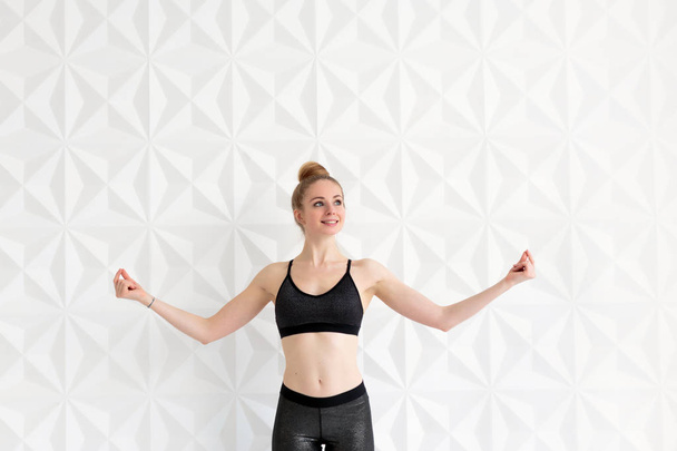 Happy fit young woman miling while posing near white wall - Photo, Image