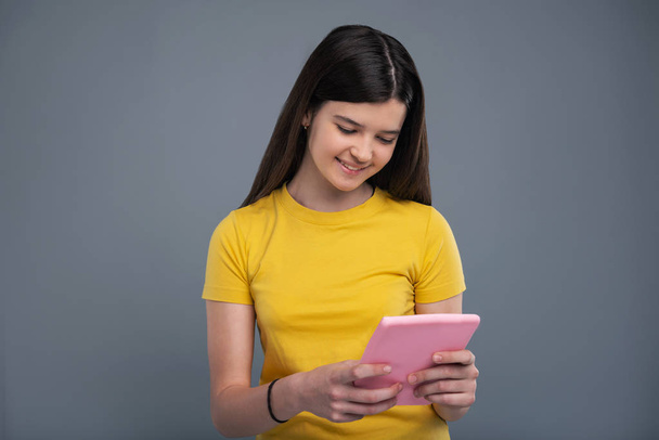 Joyeux adolescent fille en t-shirt jaune en utilisant une tablette
 - Photo, image
