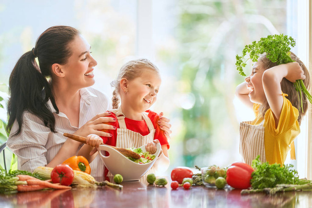 Healthy food at home. Happy family in the kitchen. Mother and children daughters are preparing the vegetables. - Foto, immagini