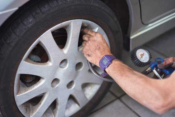 Fecho do mecânico na estação de serviço de reparação que verifica a pressão do pneu com calibre
 - Foto, Imagem