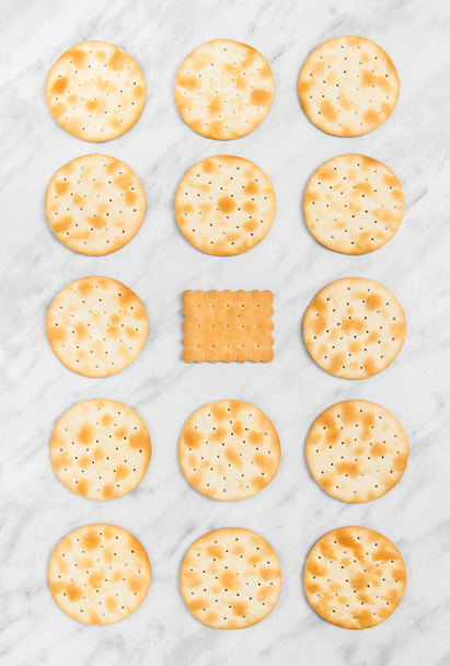 Reihen von runden Crackern und einem quadratischen Teegebäck in der Mitte, auf Marmorgrund. - Foto, Bild