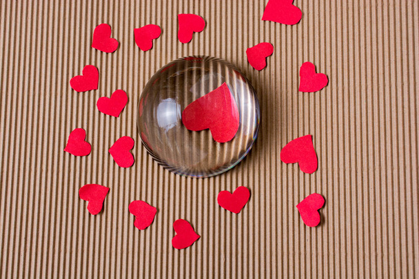 Καρδιές χαρτί κόκκινο χρώμα κάτω από και περίπου μισή γυάλινη σφαίρα - Φωτογραφία, εικόνα