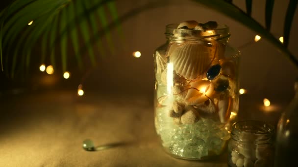 Glass jar of tropical shells for home decor. Marine style home accessories for beach themed interior decorating. - Footage, Video