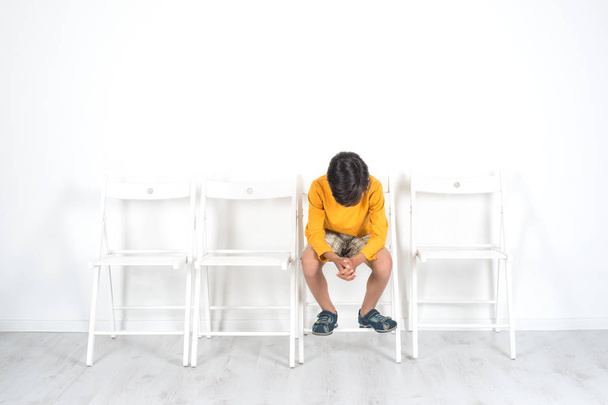 The boy sits on a chair with his head down.  He is somewhat upset and emotionally upset - Photo, Image