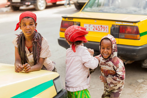 Addis Ababa, Ethiopia, January 27, 2014, Three small orphan street kids playing and laughing on a quite city road between taxis - Photo, Image