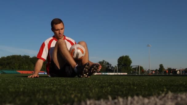 Player sitting on the grass and bouncing a soccer ball with feet - Záběry, video