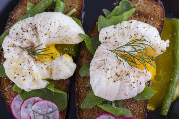 Poached egg on a piece of bread with fried green beans, radish and arugula on a plate, close up - Foto, Imagem
