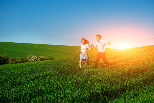 Young happy lovers running on meadow with green grass and blue sky. - Fotografie, Obrázek