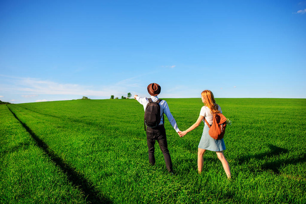 Avec un sac à dos, un homme en chapeau et une femme aux cheveux longs longent le chemin. Un couple marche le long de la prairie
. - Photo, image