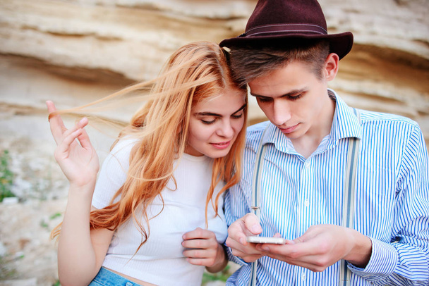 Attractive man and beautiful woman are looking at the screen of a smartphone on the background of a sand quarry. - Photo, Image