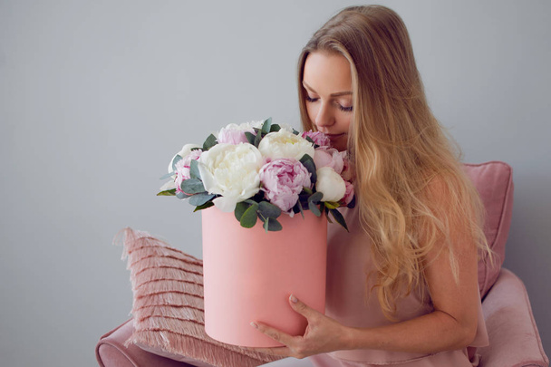 Happy blonde woman with flowers in a hat box. Bouquet of peonies. - Foto, Bild