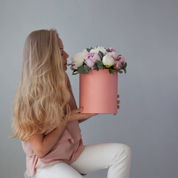 Happy blonde woman with flowers in a hat box. Bouquet of peonies. - Foto, immagini