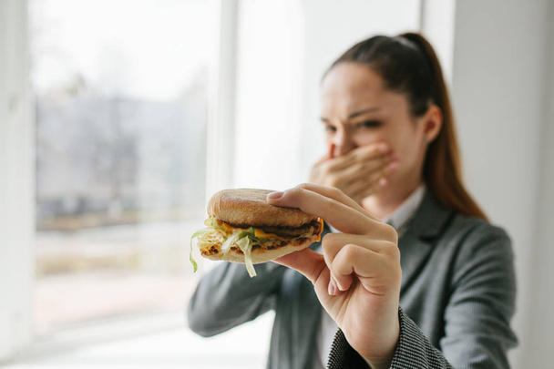 Nuori tyttö osoittaa, että hän ei pidä hampurilainen. Käsitteellinen kuva epäterveellisestä syömisestä kieltäytymisestä
. - Valokuva, kuva