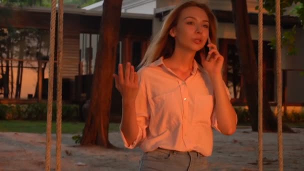 Slow motion young wife holding smartphone sitting near own mansion - Footage, Video