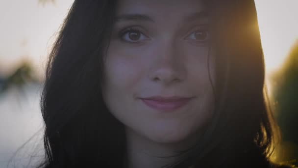 face portrait of young pretty brunette woman on a sunset background on a lake - Záběry, video