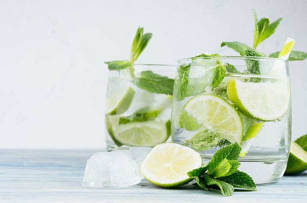 Mojito in two glasses with mint, slices lime, ice cubes, straw on soft shabby blue background, closeup. - Foto, Imagem