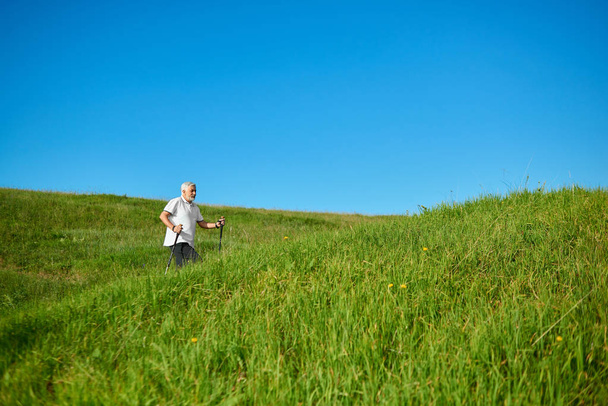 Walking with tracking sticks on fresh air between grassy hills. - Foto, afbeelding