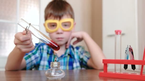 Kemiatestejä kotona. Poika lämmittää koeputkea punaisella nesteellä palavan alkoholilampun päällä. Neste kiehuu
. - Materiaali, video