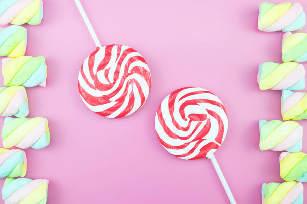 Επίπεδη θέσει το top view νόστιμο ορεκτικό έννοια, ελάχιστη marshmallow γλυκό τη θεραπεία στροβιλισμού Candy Lollipop πολύχρωμο μοτίβο σε ροζ παστέλ φόντο και αντιγράψτε χώρο - Φωτογραφία, εικόνα
