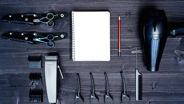 Hairdresser tools on wooden background. Blank card with barber tools flat lay. Top view on wooden table with scissors, comb, clipper and hairdryer with empty notebook and pencil, free space - Fotografie, Obrázek