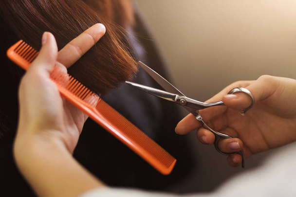 Hairdresser trimming brown hair with scissors - Fotó, kép