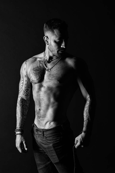 Man with tattooed arm and chest. Bearded man with strong torso. Tattoo model with sexy belly. Sportsman or athlete in fashion jeans. Bodycare with fitness and sport, black and white - Zdjęcie, obraz