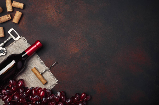Bottle of wine, red grapes, corkscrew and corks, on rusty background top view, copy space - Foto, afbeelding