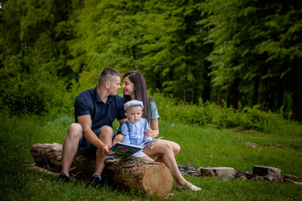 Happy mother, father and son read a book in the park. - Foto, imagen