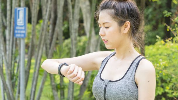 Asijské roztomilý zdravý fit a pevný štíhlý dospívající dáma pohled na smartwatch nastavit GPS nebo srdeční frekvenci před spuštěním a cvičení na venkovní zahradní park - Fotografie, Obrázek