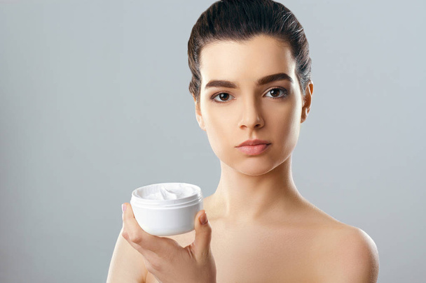 Beautiful Young Woman with Clean Fresh  Skin Holding Bottle. Beauty face care. Facial treatment. Cosmetology.Beauty and spa. - Photo, Image