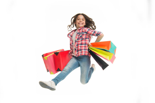Happy girl jump with shopping bags isolated on white. Little shopaholic smile with paper bags. Child shopper fashion. Shopping and sale. Birthday holiday preparation. Black friday. Fun in motion - Фото, изображение