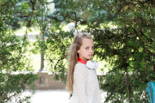 Child with long blond hair in summer park. Little girl play on fresh air outdoor. Fashion kid with headphones on nature. Summer vacation and relax. Music and modern technology - Photo, Image
