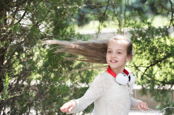 Child dancer with long flying hair. Kid dance to music in summer park. Small girl enjoy music in headphones outdoor. Melody sound and mp3. Summer fun and joy - Photo, Image
