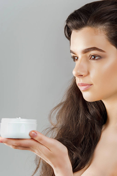 Skincare. Beauty Concept. Young pretty woman holding cosmetic cream. Soft skin and naked shoulders,model with light nude make-up, portrait of female holding moisturizing cream in her hand. Skin Protection and dermatology. - Φωτογραφία, εικόνα